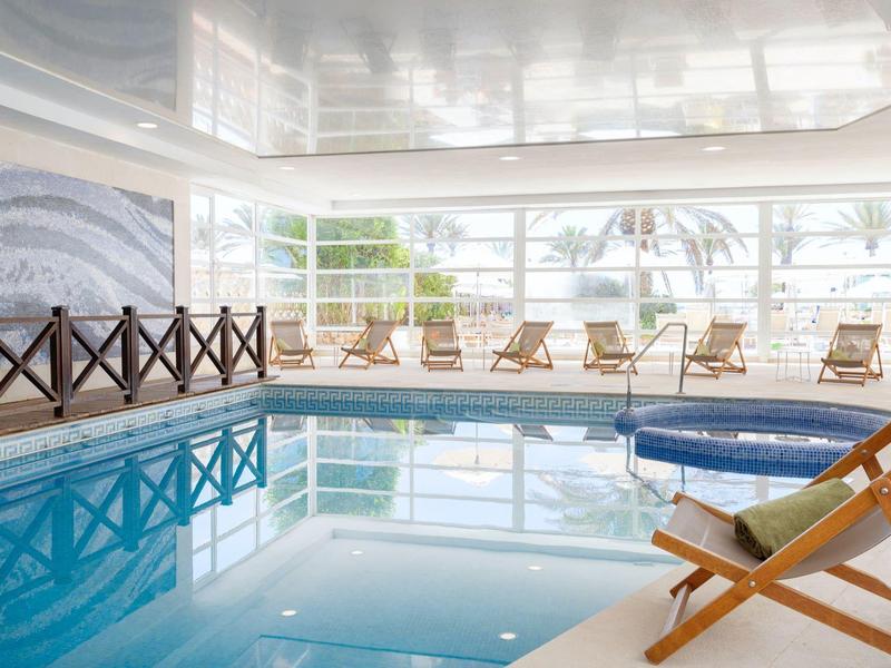 Overdekt zwembad met ligstoelen en grote ramen die daglicht binnenlaten in een hotel.