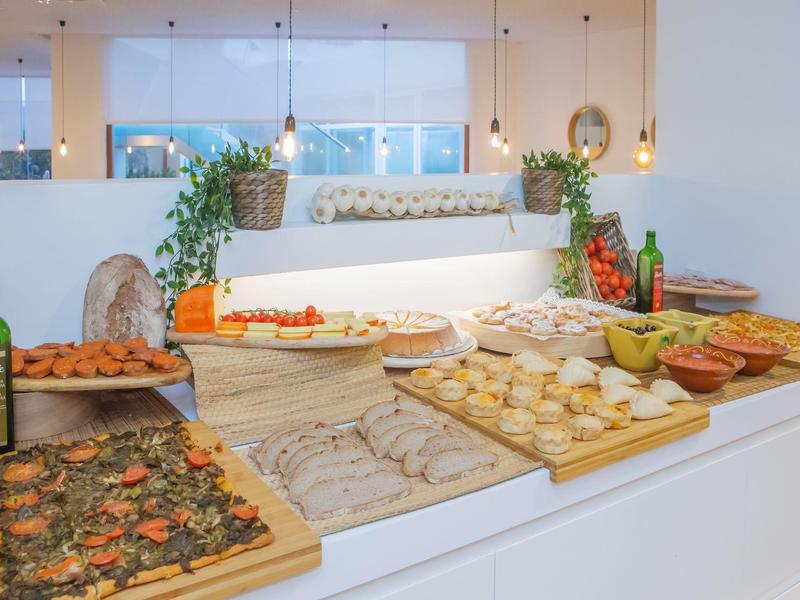 Buffet met verschillende gebakjes, broodjes en drinken in een lichte ruimte.