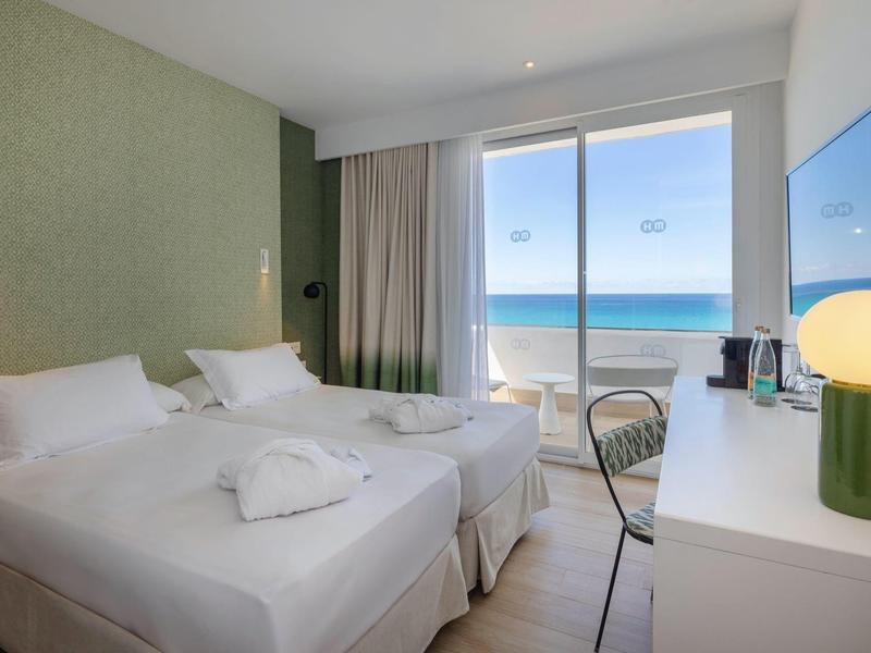 Lichte hotelkamer met twee eenpersoonsbedden en zeezicht door grote ramen.