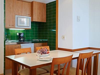 Cocina pequeña con azulejos verdes, mesa de comedor de madera y cuatro sillas.