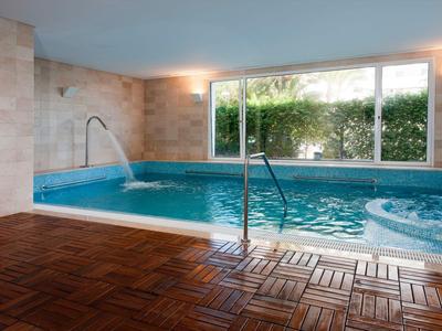 Piscina interior con fuente de agua, jacuzzi y grandes ventanas con vistas al jardín en un hotel.