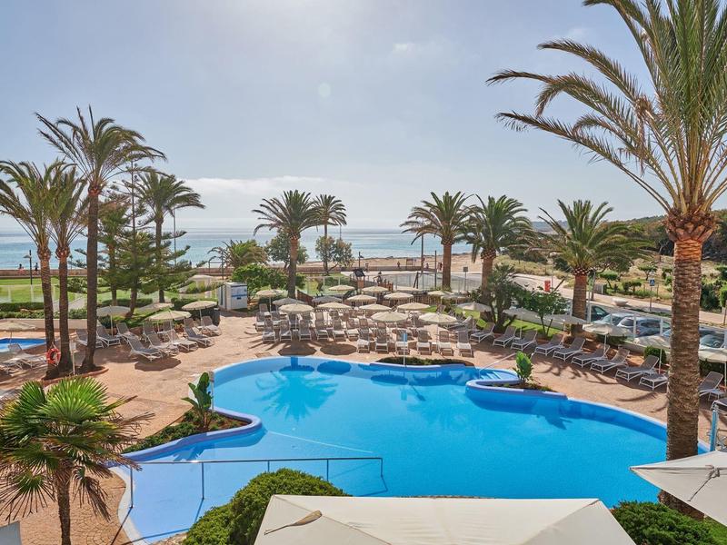 Área de piscina lujosa con palmeras y vista al mar en un complejo hotelero.