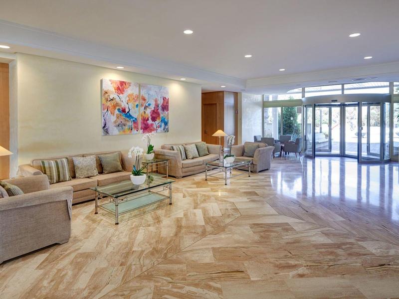 Lobby de hotel luminosa con suelo de mármol, sofás cómodos y pintura colorida en la pared.