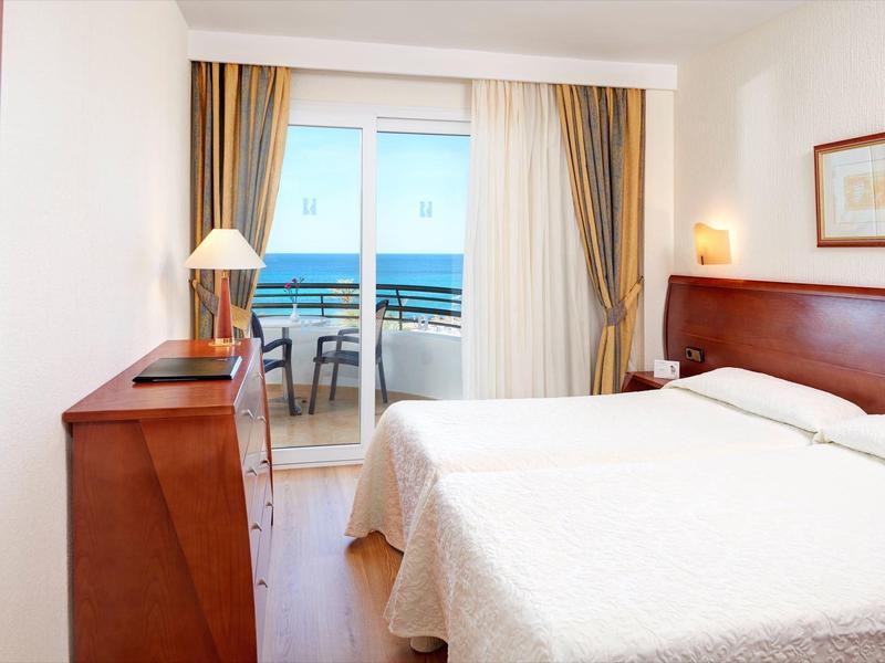 Habitación de hotel luminosa con cama doble, muebles de madera y balcón con vista al mar.