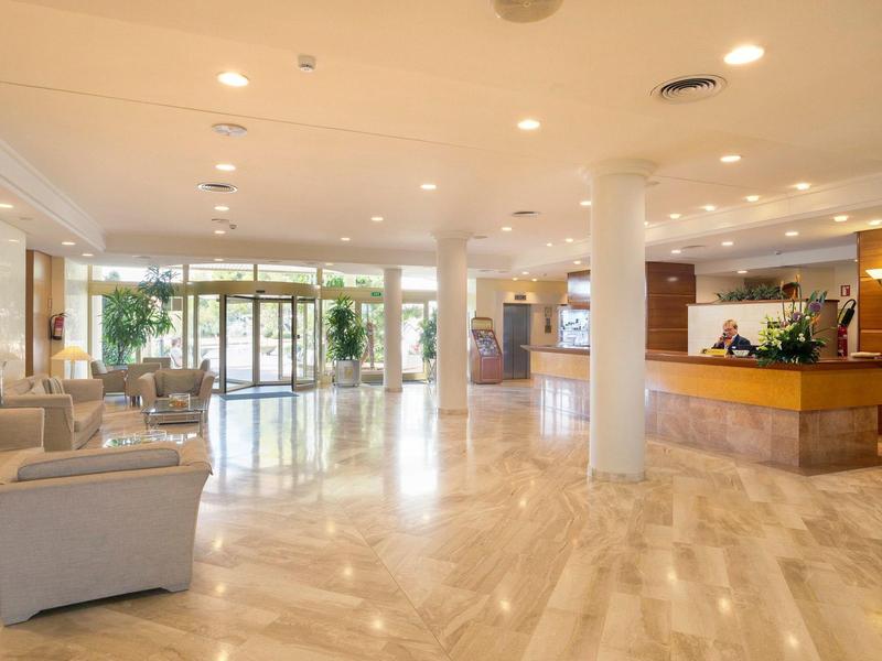 Lobby de hotel luminosa con suelo de mármol, recepción y zona de asientos con sofás cerca de la entrada.