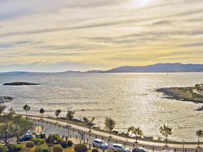 Vue sur une promenade côtière avec des palmiers, une plage et des montagnes en arrière-plan au coucher du soleil.