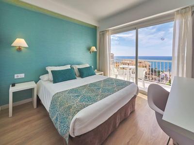 Chambre d'hôtel moderne avec lit double, mur turquoise et vue sur la mer à travers de grandes fenêtres.