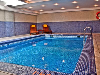 Piscine intérieure avec carrelage bleu, deux chaises et une bouée de sauvetage d'urgence au mur.