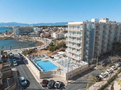 Vue d'un bâtiment hôtelier avec piscine extérieure et parkings environnants près de la plage.