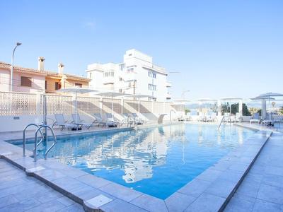 Piscina esterna moderna con acqua blu limpida e edifici bianchi sullo sfondo.