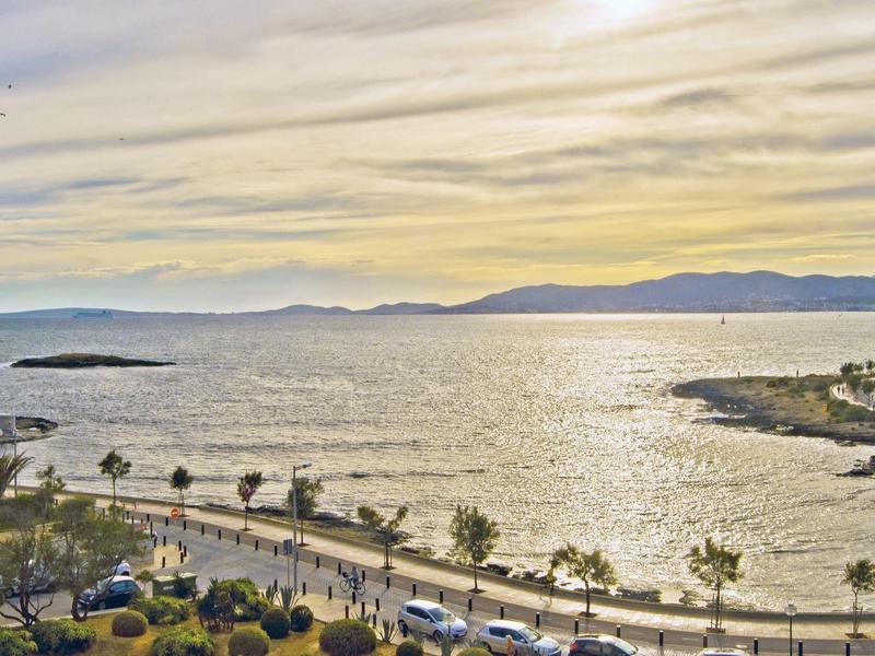 Vue sur une promenade côtière avec des palmiers, une plage et des montagnes en arrière-plan au coucher du soleil.