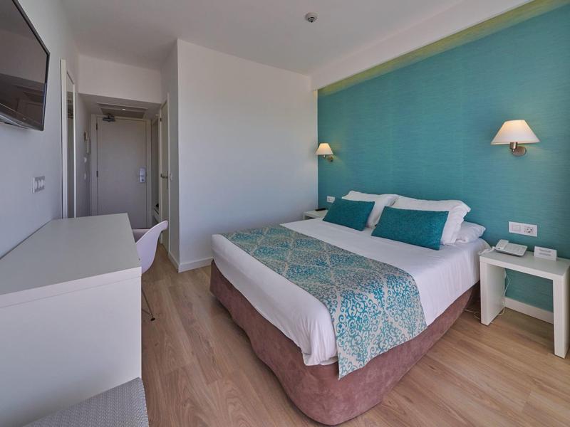 Chambre d'hôtel moderne avec lit double, mur turquoise, bureau et télévision.