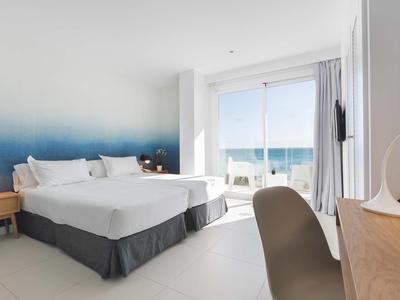 Modern hotel room with large beds and sea view through a glass sliding door.
