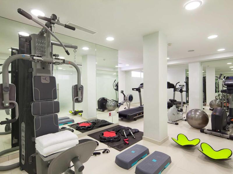 Modern gym equipment in a well-lit fitness room with mirrors and accessories.