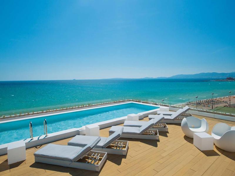 Modern pool with sun loungers and seating overlooking the sea and blue sky.