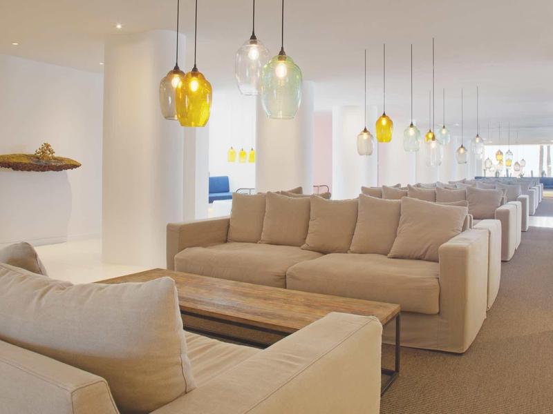 Bright, modern lounge area with beige sofas and hanging colorful lamps in a hotel.