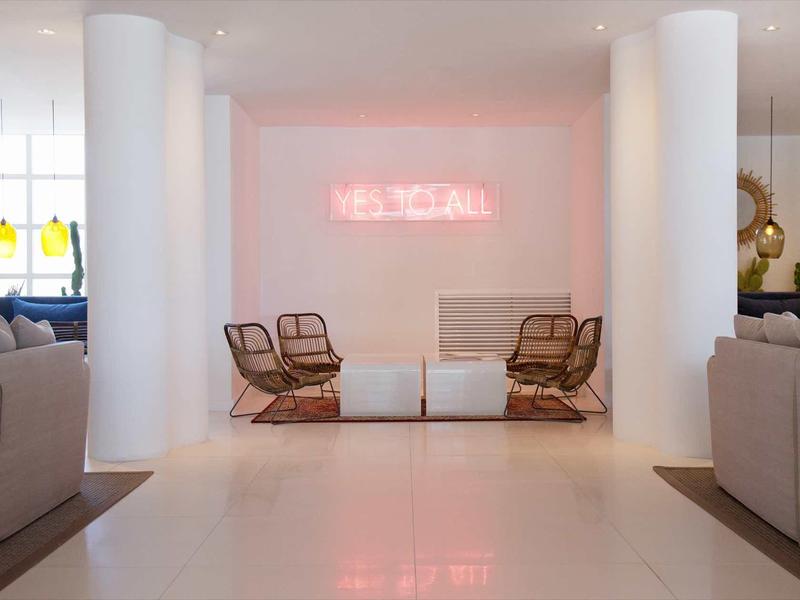 Modern hotel lounge area with chairs, sofas, and pink neon light on the wall.