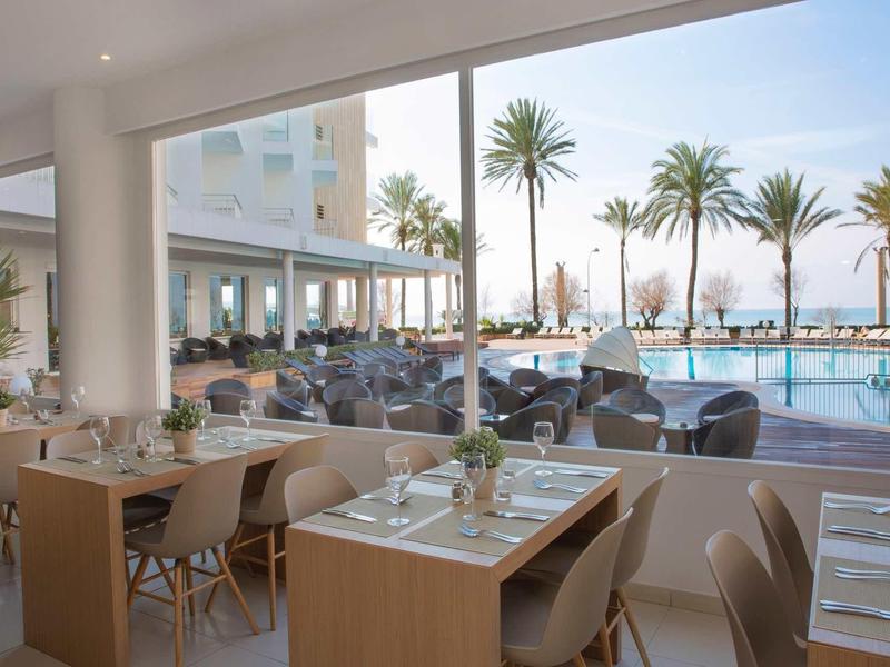Modern hotel restaurant area overlooking pool and palm trees.