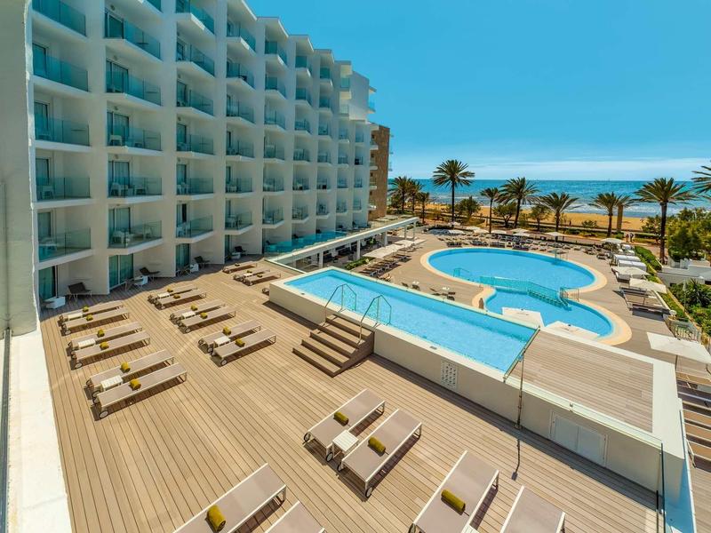Hotel with pool, sun loungers, and sea view under clear sky.