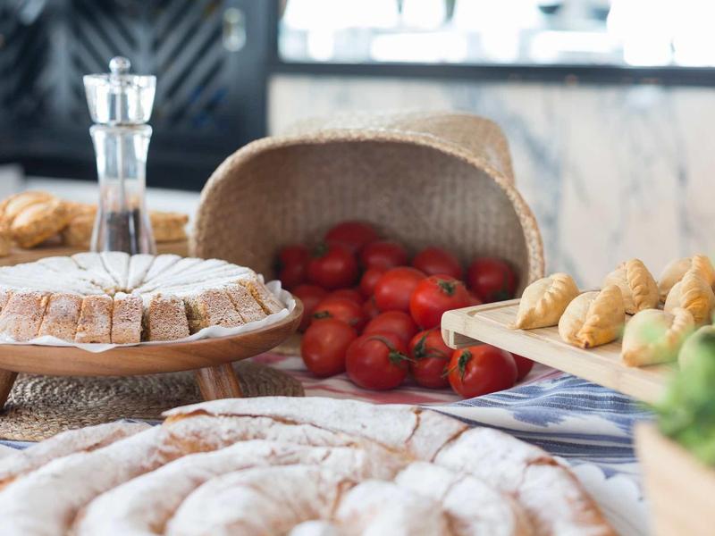 Buffet with pastries, tomatoes, and herbs on a table in a bright kitchen.
