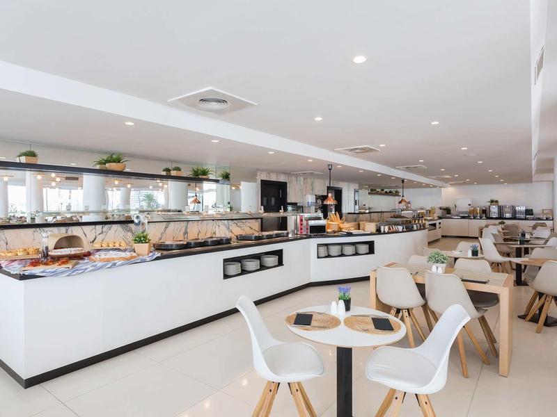 Modern, bright restaurant with buffet area and tables with white chairs.