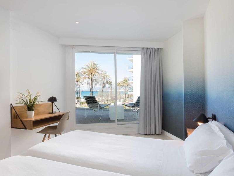 Bright hotel room with sea view through large windows leading to terrace.