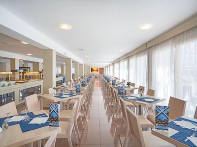 Ristorante d'hotel luminoso e moderno con lunghe file di tavoli e sedie, tovagliette blu e grandi finestre.