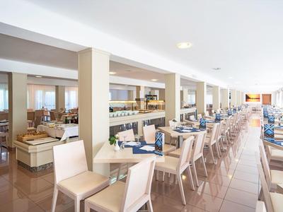 Lichte, ruime hotel eetzaal met netjes opgestelde tafels en stoelen in rijen.