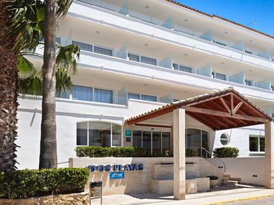 Vier verdiepingen tellend wit hotel met balkons, palmbomen en een overdekte ingang.