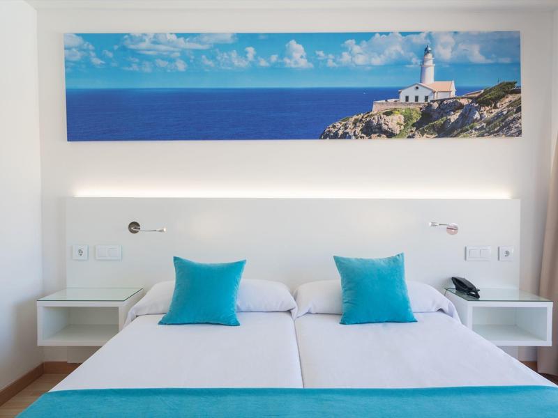 Moderne hotelkamer met twee eenpersoonsbedden, blauwe kussens en zeezicht kunstwerk boven.