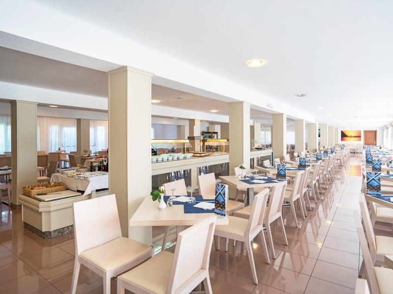 Lichte, ruime hotel eetzaal met netjes opgestelde tafels en stoelen in rijen.