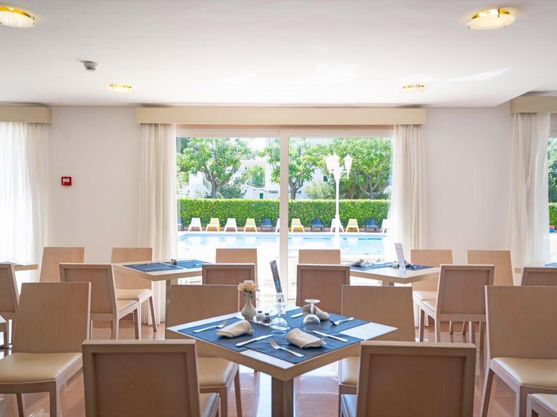 Lichte eetkamer met houten stoelen en tafels gedekt voor maaltijden bij grote ramen.