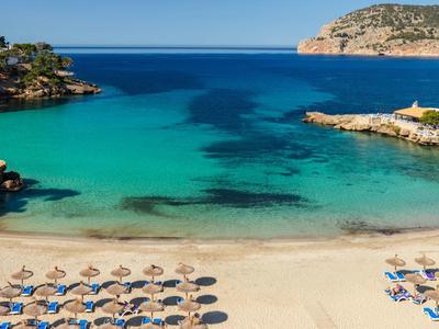 Clear blue sea with a sandy beach and rows of umbrellas and sunbeds.