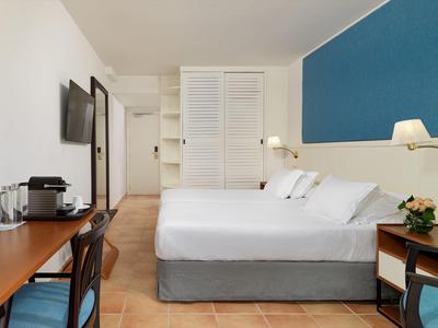 Modern hotel room with double bed, blue accent wall, desk, chair, and coffee machine.