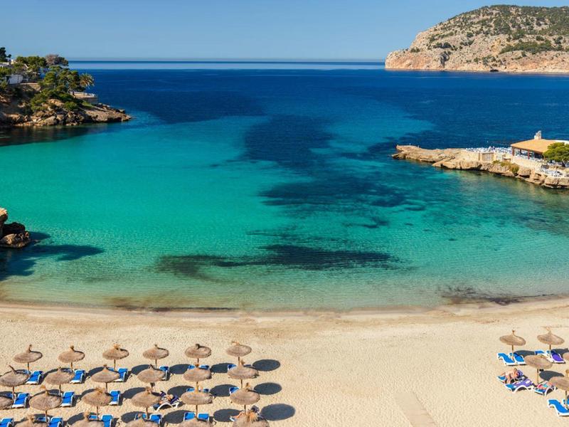 Clear blue sea with a sandy beach and rows of umbrellas and sunbeds.
