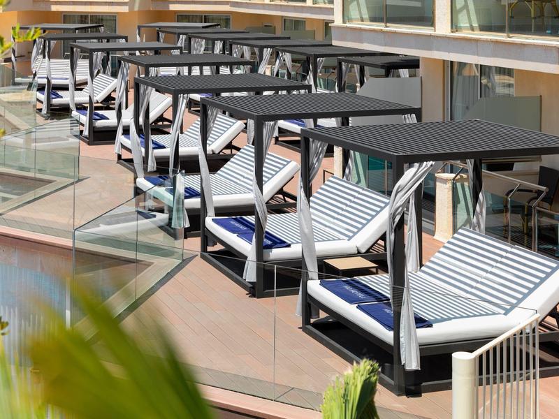 Outdoor hotel balcony seating with black tables and striped cushions overlooking greenery.