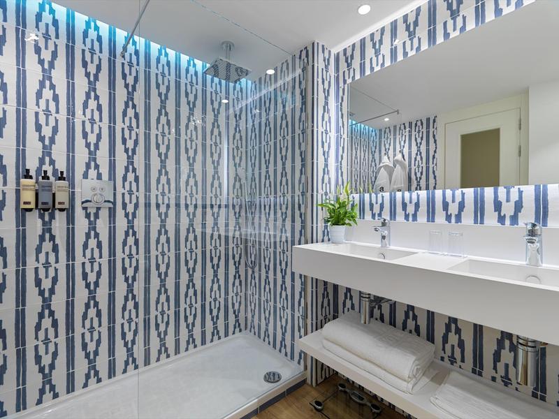 Modern bathroom with blue-patterned wall tiles, glass shower, white sink, and large mirror.