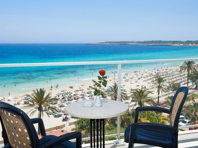 Balkon met tafel en stoelen met uitzicht op een druk zandstrand en blauwe zee.
