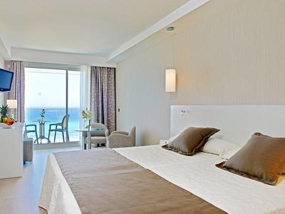 Licht hotelkamer met zeezicht, balkon en tweepersoonsbed.