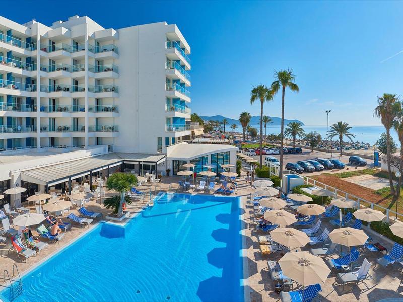 Moderne hotelzwembad met ligstoelen, parasols en zeezicht onder een heldere hemel.