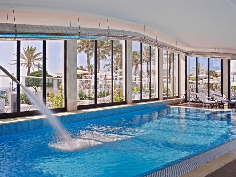 Lichtovergoten binnenzwembad met waterval en panoramische ramen.