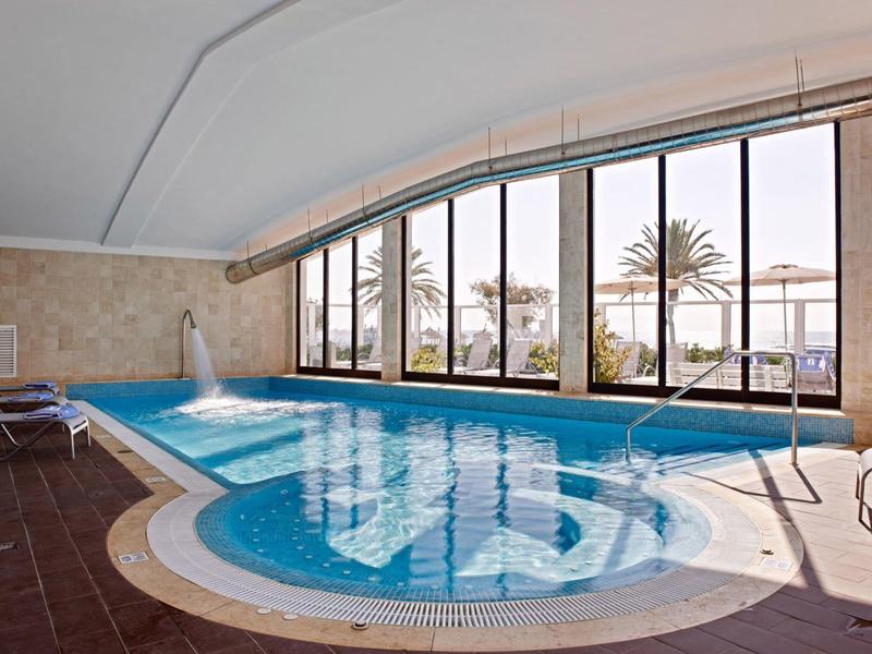 Overdekt zwembad met grote ramen en uitzicht op palmbomen buiten.