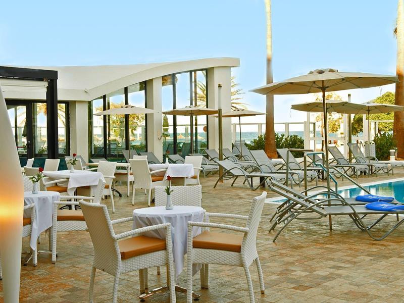 Moderne buitenruimte met zwembad, tafels en parasols bij een hotel.