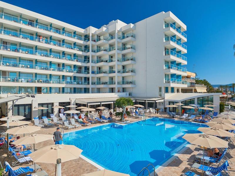 Modern hotel met groot zwembad, ligstoelen en parasols onder een heldere hemel.