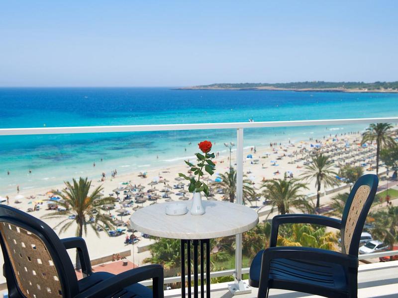 Balkon met tafel en stoelen met uitzicht op een druk zandstrand en blauwe zee.