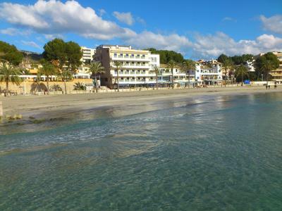 Strand met helder water en hotelgebouwen op de achtergrond onder een blauwe lucht