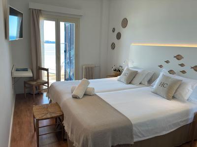 Lichte hotelkamer met tweepersoonsbed, houten vloer en balkon met zeezicht.