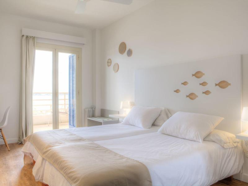 Světlo ložnice se dvěma jednolůžky, bílými stěnami a výhledem na balkon.