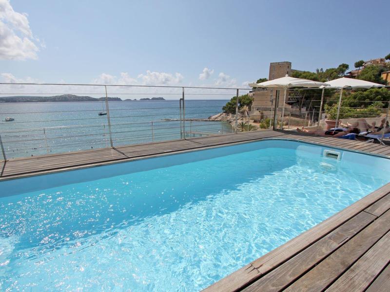 Malý bazén s dřevěnou terasou s výhledem na moře a slunečníky vedle hotelové terasy.