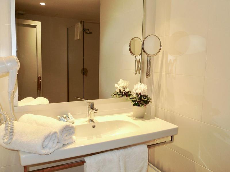 Moderní hotelové koupelnové umyvadlo se zrcadlem, ručníky a květinou.